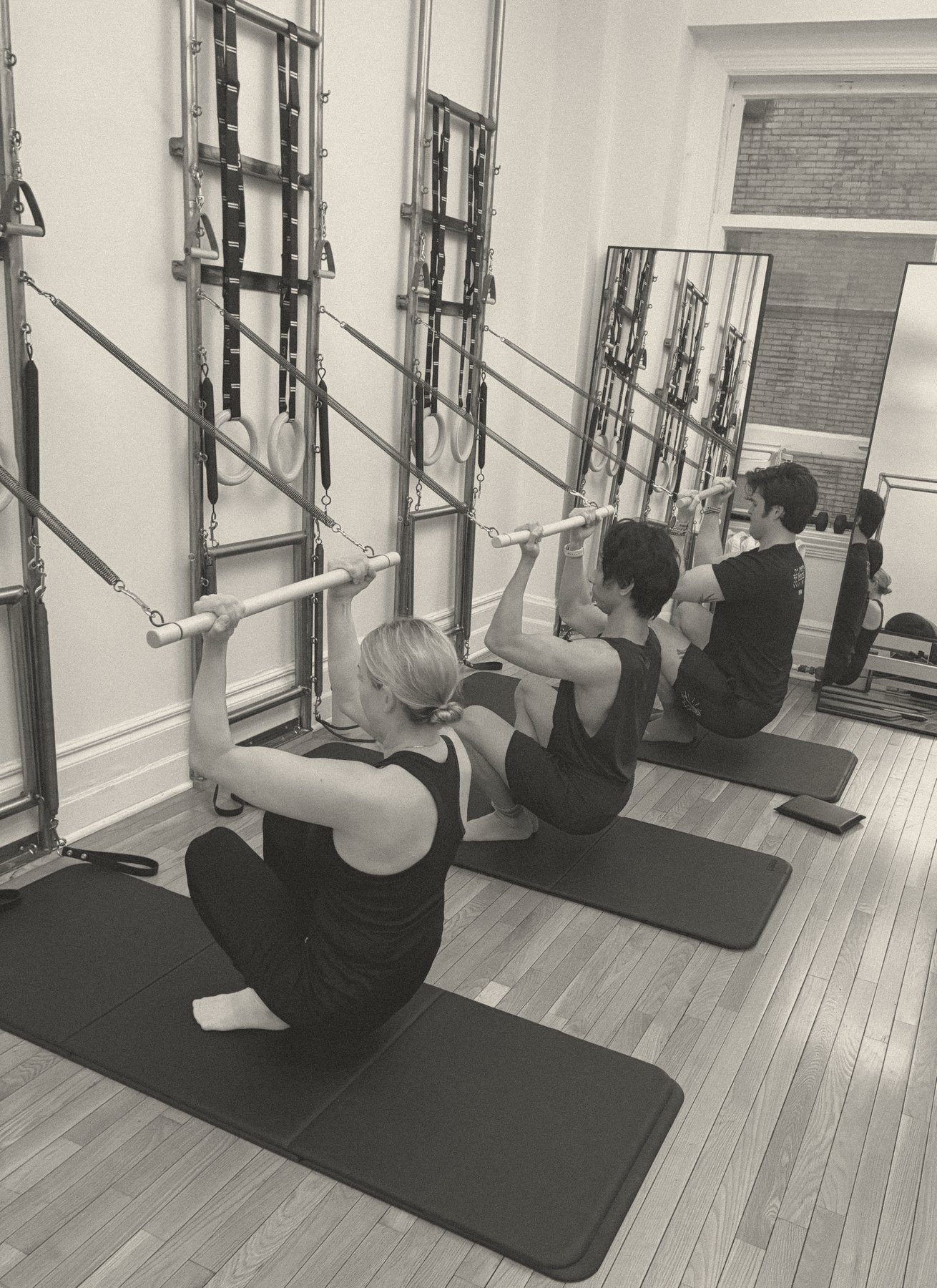 Three clients on mats working with spring-loaded bars at the wall units, semi-private Pilates class at Will Taylor Studio